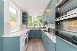 cocina con armarios azules, lavadora y secadora en Stylish & Spacious 3-Bed House, Parking and Garden, en Finchley