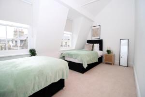a white bedroom with two beds and a window at Heart of Bath: Kingsmead Apartment in Bath