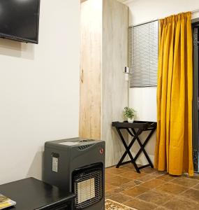 Zimmer mit Heizung, Tisch und gelben Vorhängen in der Unterkunft Olive Tree Studio Apartment in Harrismith
