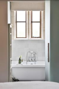 ein weißes Badezimmer mit einem Waschbecken und zwei Fenstern in der Unterkunft Cotswold Luxury Coach House - ideal for couples, w/ EV charging in Andoversford