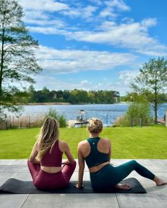 two women sitting on the ground looking at the water at Boskata Spa & Wellness Resort Ślesin in Mikorzyn