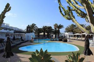 una piscina en un complejo con palmeras y sombrillas en Lanzarote Club Tahiti - July 11, 2024 until July 17, 2024 en Costa Teguise