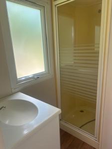 La salle de bains blanche est pourvue d'un lavabo et d'une douche. dans l'établissement Camping Le Ruisseau, à Saint-André-de-Seignanx