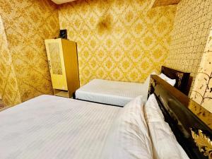 Jhelum Khan Hotel في Jhelum: سريران في غرفة صغيرة مع ورق جدران أصفر