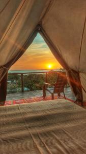 uma tenda com uma cama e um banco em frente a um pôr-do-sol em Puerta al Mar Ecolodge Glamping em Tubará