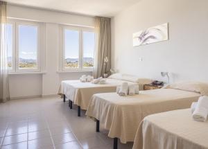 Habitación con 4 camas, sábanas blancas y ventanas. en Hotel De Plam en Olbia