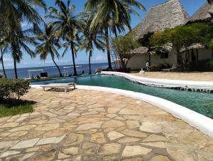 een zwembad naast een strand met palmbomen bij MARIA the Star on the Sea Beach cottages, cottage Mama in Malindi