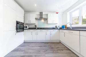 cocina blanca con armarios blancos y suelo de madera en TMW guest house en Thamesmead