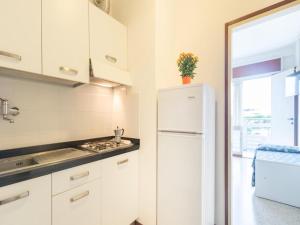La cuisine est équipée de placards blancs et d'un réfrigérateur blanc. dans l'établissement Cozy studio apartment with sea view - Beahost, à Lignano Sabbiadoro