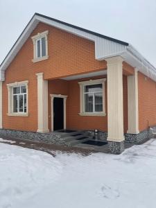 a red brick house with a porch in the snow at Guest house with mountain view in Pokrovka