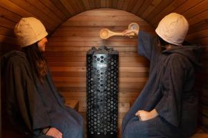 dos personas sentadas en una sauna con un termómetro en 丘の上から海が見える一棟貸しヴィラ しまいろ長手, 