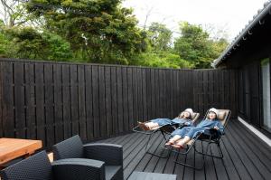 two women are sitting in chairs on a deck at 丘の上から海が見える一棟貸しヴィラ しまいろ長手 