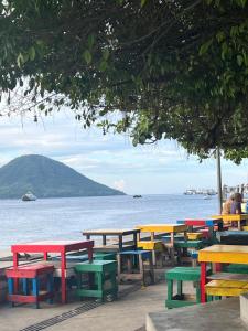 una fila de mesas y bancos coloridos junto al agua en KBI Hostel, en Ternate