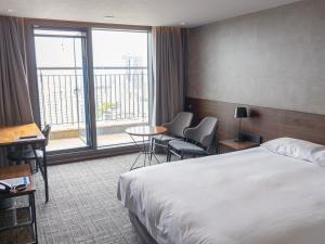 済州市にあるHotel With Cityのベッドと大きな窓が備わるホテルルームです。