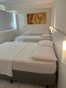 a row of beds in a room with white sheets at Pousada Oceanic in Arraial do Cabo