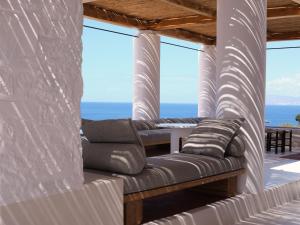 a couch on a porch with the ocean in the background at Boheme Mykonos Town - Small Luxury Hotels of the World in Mikonos
