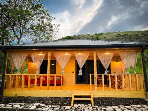 Cette maison en bois dispose de rideaux et d'une terrasse couverte. dans l'établissement Teo's Cottages, à Dedoplis Tskaro