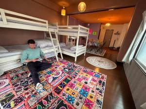 a man sitting on a rug in a room with bunk beds at 777 Takamatsu Guest House in Takamatsu