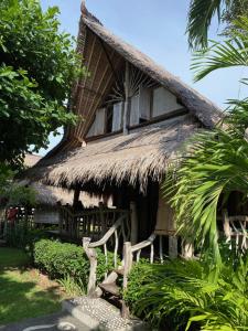 una casa con tetto di paglia e panca davanti di Flower Bud Bungalow Balangan a Jimbaran