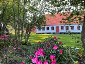 uma casa branca com um telhado vermelho e flores cor-de-rosa em Country Idyll With Wilderness Bath And Sauna, em Haderslev