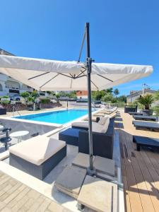 a pool with a white umbrella and chairs and a swimming pool at Apartments Silva in Trogir