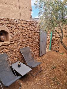 two chairs and a table in front of a stone wall at Ksar Montana Gîtes, Chambres piscine in Taforhalt