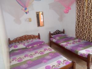 2 Betten in einem Zimmer mit rosa und lila Bettwäsche in der Unterkunft Kunam Beach Rest Inn in Batticaloa