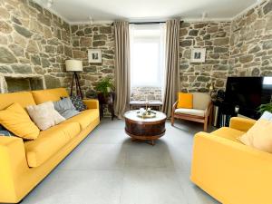 a living room with yellow furniture and a stone wall at Old stone house Klarić in Brela