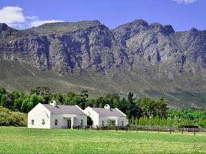 two white buildings in a field with mountains in the background at Auberge La Dauphine Guest House in Franschhoek