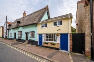 une maison jaune et bleue sur le côté d'une rue dans l'établissement Wits End Cottage, à Mildenhall