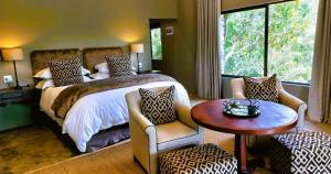 1 dormitorio con 1 cama, mesa y sillas en African Safari Lodge, en Grahamstown