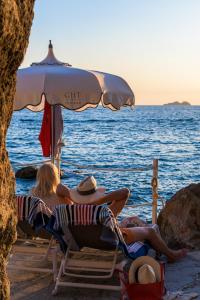 普萊伊亞諾的住宿－特里托尼大酒店，两人坐在海滩上一把遮阳伞下的椅子上