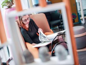a woman sitting in a chair reading a newspaper at Novotel Suites Luxembourg in Luxembourg