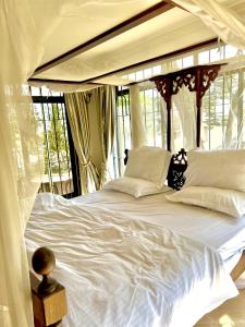 uma cama com lençóis brancos e almofadas num quarto com janelas em Wenzi Luxury Home em Arusha
