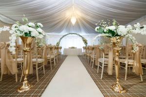 a wedding aisle with chairs and flowers in a marquee at Heritage Park Pontypridd, Trademark Collection by Wyndham in Pontypridd