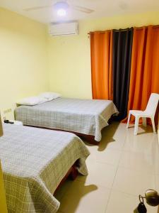 two beds in a room with orange curtains and a chair at Hotel Vista Sur in Los Patos