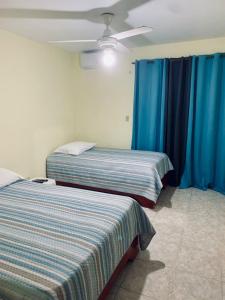 2 camas en una habitación con cortinas azules y ventilador de techo en Hotel Vista Sur, en Los Patos