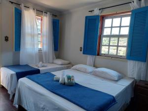 2 camas en una habitación con ventanas con persianas azules en Pousada Ouro Preto en Ouro Preto