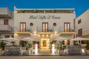 a hotel with tables and umbrellas in front of a building at Hotel Soffio D'Estate in San Vito lo Capo