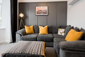 uma sala de estar com um sofá cinzento e almofadas amarelas em Dunraven by StayStaycations em Port Talbot