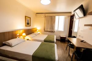 a hotel room with two beds and a desk at Hotel Golden Star in Curitiba