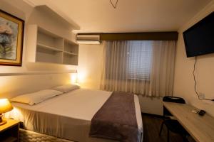 een slaapkamer met een bed, een bureau en een raam bij Hotel Golden Star in Curitiba