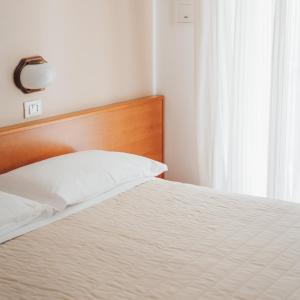 un letto con testiera in legno e cuscino bianco di Hotel Jesulum a Lido di Jesolo