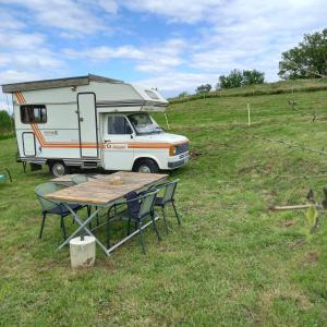 uma caravana estacionada num campo com uma mesa e cadeiras em Camping car vintage em Saint-Barthélemy-le-Plain