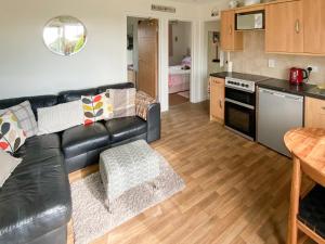 a living room with a black leather couch and a kitchen at Barn Owls Holiday Bungalow in Salcombe Regis