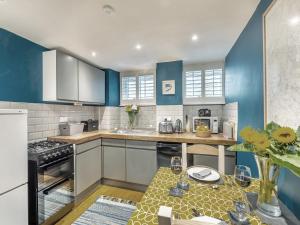 uma cozinha com paredes azuis e armários brancos e uma mesa em Castlebergh Cottage em Settle