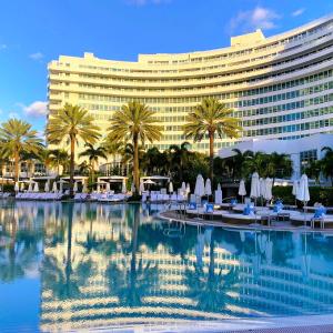 a hotel with a pool with chairs and palm trees at Luxury King apartment with Bay View at Miami Beach in Miami Beach