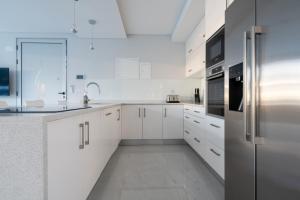 una cocina blanca con armarios blancos y electrodomésticos de acero inoxidable en Villa Pérola, en Calheta