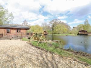 a log cabin with a playground next to a lake at Woodpecker Lodge in Langham
