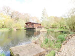 a wooden bridge over a lake with a house at Wagtail Lodge in Langham